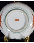 Close-up of the underside of an antique Japanese Satsuma porcelain plate with red hand-painted designs and a red stamp.