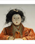 Close-up of an antique Japanese Taisho samurai doll with a white face, black hair, ornate orange-gold kimono from Kyoto.