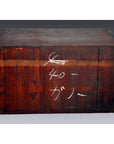 Close-up of antique red-toned wooden Japanese Tansu with worn finish and white Japanese chalk writing on the front.