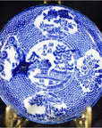 White porcelain Japanese transferware plate with floral and landscape designs on decorative metal stand, close-up view.