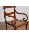 Brown wood and rattan armchair with carved back and curved arms, set against a white brick wall indoors.