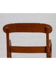 Brown wooden and rattan armchair with carved back and curved arms, shown indoors against a white brick wall.