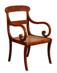 Brown wooden and rattan armchair with carved back and curving arms, antique Javanese style, indoor setting.