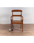 Brown wood and rattan armchair with carved back and curved arms on wood floor against white brick wall indoors.