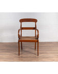 Brown wooden Javanese armchair with carved back, curved arms, and rattan seat on a wooden floor indoors.