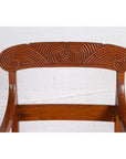 Close-up of brown wooden Javanese armchair backrest with carved swirl patterns on the top rail.