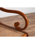 Brown wooden and rattan armchair with carved back and curved arms, on wood floor against white wall indoors.