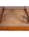 Close-up of brown wooden Javanese armchair with carved back, curved arms, and rattan seat on wood floor.