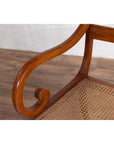 Brown wood and rattan armchair with carved back and curved arms on a wooden floor.
