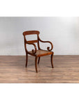 Brown wooden and rattan Javanese armchair with carved back and curved arms, on wood floor by white brick wall indoors.