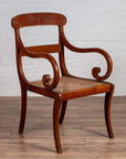 Brown wood and rattan armchair with carved back and curving arms on a wooden floor indoors.