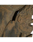 Close-up of brown teakwood Burmese temple carving, mirrored guardian relief with stylized headgear.