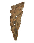 Brown wood temple carving, mirrored guardian relief with stylized headgear and intricate patterns, close-up view.