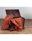 Open brown wooden blanket chest with gilt accents, draped in red and gold patterned fabric.