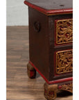 Brown hand-carved wooden blanket chest with gilt accents, metal handle, and decorative legs on a wooden floor.