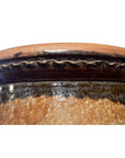 Close-up of brown ceramic rim and upper edge of antique Martaban water jar with wavy decorative pattern.