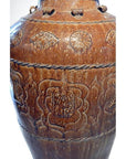 Brown ceramic Martaban water jar with floral patterns and textured bands, close-up view.