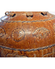 Brown ceramic water jar close-up with embossed geometric and floral patterns, textured surface visible.