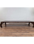 Dark wood opium bed with curved legs on wooden floor against white brick wall, antique Northern Chinese Ming Dynasty style.