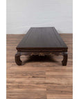 Brown wood Ming Dynasty style Kang opium bed on a brown wood floor, set against a plain white wall indoors.