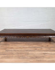 Dark wood Ming dynasty style Kang opium bed with hand-carved legs on light wood floor against white brick wall indoors.