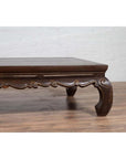 Dark wood low opium bed with curved legs on hardwood floor against white brick wall indoors.