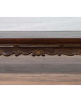 Close-up of a dark wood hand-carved edge on an antique Ming Dynasty style opium bed near a light wall and floor.