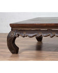 Close-up of dark wood Northern Chinese Ming Dynasty style bed with hand-carved frieze and scalloped apron indoors.