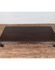 Dark wood Chinese Ming Dynasty style opium bed with curled legs on a wood floor against a white wall indoors.
