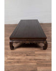 Wooden Northern Chinese Ming style opium bed with hand-carved legs on a wooden floor against a white wall indoors.