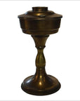 Close-up of antique brass oil lamp with round base, slender stem, and wide lidded reservoir.