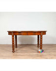 Brown wood antique oval dining room table with spindle legs, warm patina, on wood floor by white brick wall.