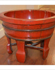 Antique red lacquer wash basin with wide rim and curved legs on a wooden floor indoors.