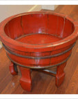 Antique red lacquer wash basin with four curved legs on hardwood floor next to beige wall.