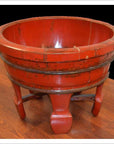 Antique red lacquer wash basin with wide rim and four legs on polished wooden surface, close-up.