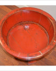 Antique red lacquer wash basin with rustic finish on wood floor next to a white wall.