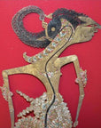 Close-up of antique leather shadow puppet with intricate carvings on a vibrant red background.