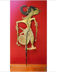 Gold and red leather Indonesian shadow puppet, close-up, displayed against a vibrant red background.