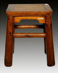 Close-up of rustic elm wood antique stool with four legs and square seat, set against a gradient dark background.