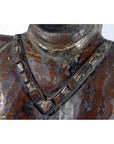 Close-up of antique Sumatra fertility mask, dark-toned material, with square-patterned necklace and shoulders visible.