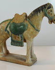 Glazed terracotta horse with green saddle from Ming Dynasty on rectangular base, close-up view.