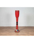 Red wood ceremonial drum with round base on a wood floor next to a white wall indoors.