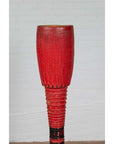 Red wood ceremonial drum with round base, placed indoors against a white brick wall.