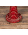 Red wood ceremonial drum with round base on wooden floor, white border in background, indoor setting.