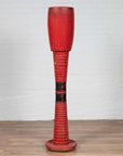 Red wood freestanding Thai ceremonial drum with round base on wooden floor next to white brick wall indoors.