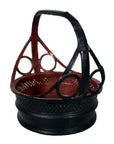 Close-up of a round black and red basket with a tall geometric handle and circular cut-out designs, woven material.