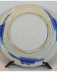 Close-up of the white porcelain ARITA MEIJI plate back with blue brushstrokes on a black display stand.