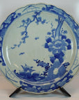 Blue and white porcelain plate with hand painted floral and bird design, displayed on a black stand.