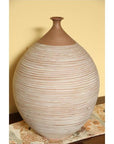 Large ceramic vase with thin stripes on patterned cloth, yellow wall background, indoor setting.