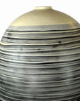White ceramic vase with rounded top and black-gray stripes, close-up against a plain background.